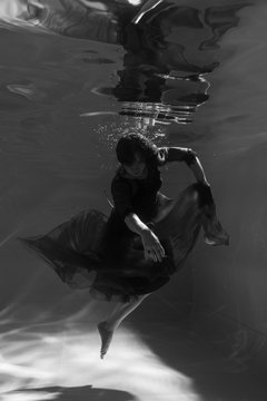 Black and white photo. Beautiful girl underwater in a red dress swims in the pool. Tenderness and elegance. Bubbles and a lot of water