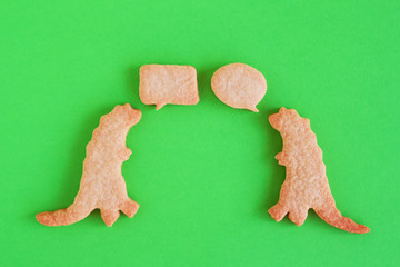 Homemade shortbread cookies in shapes of dinosaurs with callout clouds on green background, top view.