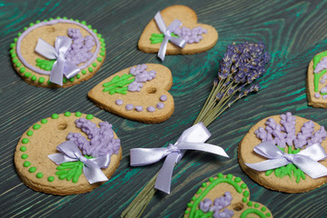 Gingerbread cookies decorated with glaze. On some ribbons tied to a bow. Gingerbread cookies are round and in the shape of a heart. Near a bouquet of lavender. On brushed pine boards.