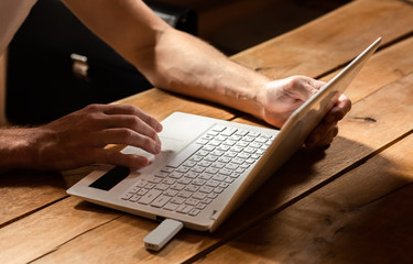 Male's hands typing at white laptop on a wooden table