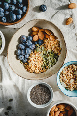 Top view of a morning granola and ingredients like almond, blueberry, pepitas and chia seeds on a linen cloth.