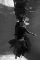 Black and white photo. Beautiful girl underwater in a red dress swims in the pool. Tenderness and elegance. Bubbles and a lot of water