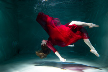 Beautiful girl underwater in a red dress swims in the pool. Tenderness and elegance. Bubbles and a lot of water