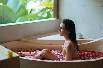 Woman relaxing in stone bath tube with tropical flowers with jungle view, organic skin care, luxury spa hotel, Bali Indonesia