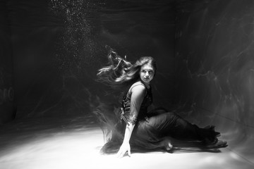 Black and white photo. Beautiful girl underwater in a red dress swims in the pool. Tenderness and elegance. Bubbles and a lot of water