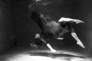 Black and white photo. Beautiful girl underwater in a red dress swims in the pool. Tenderness and...