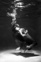 Black and white photo. Beautiful girl underwater in a red dress swims in the pool. Tenderness and elegance. Bubbles and a lot of water
