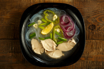 A plate of Vietnamese pho soup with chicken on a wooden table.