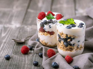 White yogurt in glass jar with fruits on grey background.