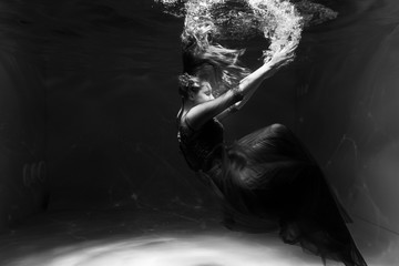 Black and white photo. Beautiful girl underwater in a red dress swims in the pool. Tenderness and...