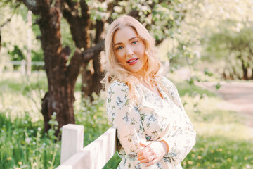 Portrait beautiful tender woman in stylish white floral retro dress on green summer garden. Young attractive hippie girl with wavy hair posing in countryside park and smile. Enjoy nature and relax