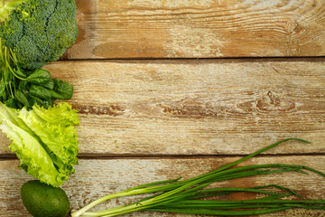 Green vegetables, broccoli, avocado, onions, spinach on the edge of a table of rough boards.