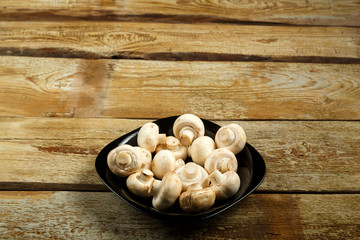Champignons in a black plate on a table of rough boards.