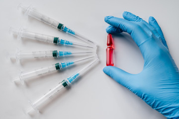 A hand in a latex blue glove holds a red ampoule with a cure for the disease, syringes for a set of...