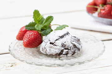 Homemade chocolate crinkles and strawberry in a glass saucer.