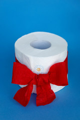 Toilettenpapier Rolle mit roter Geschenk-Schleife vor blauem Hintergrund