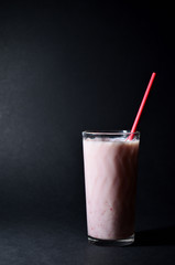 milkshake with strawberry syrup in a glass glass with a red paper tube on a black background With copy space