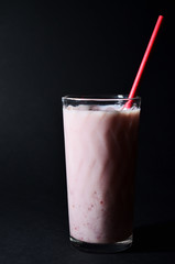 milkshake with strawberry syrup in a glass glass with a red paper tube close-up