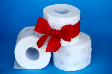 Toilettenpapier Rollen mit Blumen Muster und roter Geschenk-Schleife vor blauem Hintergrund