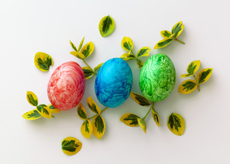 Colorful Easter holiday eggs, arranged with green twigs and an orange wreath of grass on a white background.
