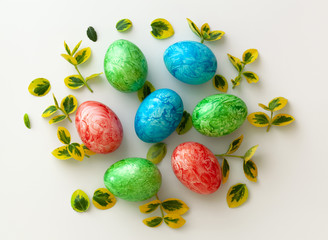 Colorful Easter holiday eggs, arranged with green twigs and an orange wreath of grass on a white background.