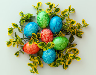 Colorful Easter holiday eggs, arranged with green twigs and an orange wreath of grass on a white background.