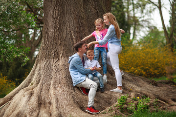 Naklejka na ściany i meble Young family with two children daughter and son in botanical garden summer city park have a rest near tree in nature