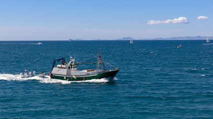 Fototapeta na wymiar A fishing trawler returns from fishing to the port of the Spanish city of Torrevieja. There are also sailing boats on the Mediterranean. Mountains can be seen in the background in the south.