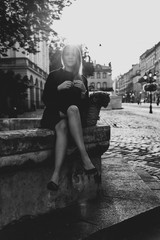 Fototapeta na wymiar .beautiful young woman in a black dress with blond hair sits on a fountain with a bag in which red flowers