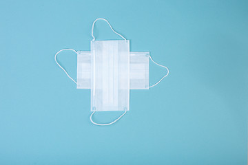 healthcare, medicine and charity concept: white cross symbol made from two white surgical masks for protection from COVID-19 isolated on blue background