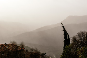 A picturesque landscape view of the hazy Pyrenees mountain range on a rainy and windy morning (Hautes-Pyrenees, France)