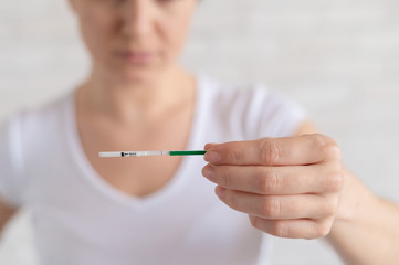 A frustrated woman shows a negative pregnancy test. The concept of female infertility. Human chorionic gonadotropin. One strip. Unjustified expectations.