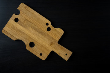Cutting board made of light wood with cheese-like holes on a dark wooden background, text area, top view.