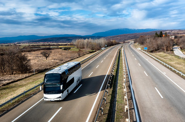 White Modern comfortable tourist bus driving through highway at bright sunny sunset. Travel and...