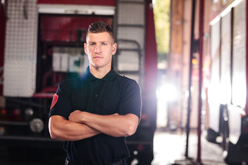 Obraz premium Professional fireman portrait. Firefighter wearing shirt uniform and fire truck in the background.
