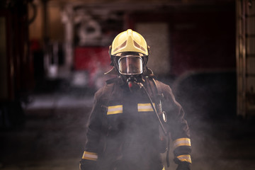 firefighter portrait wearing full equipment with oxigen mask. fire trucks in the background.