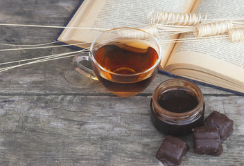 Cup of tea with open book and chocolate sweets on wooden background.