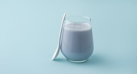 glass of blue matcha latte and white spoon on blue background
