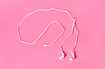 Portable white headphones for smartphone or audio player on pink background