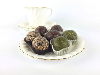 Energy balls which are booster food are set on a white plate in front of a white tea cup and isolated on white background.