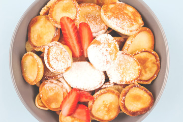 Close up of mini pancakes cereal with strawberries in blue bowl for breakfast as new trendy food activities during coronavirus quarantine lockdown. Healthy breakfast for children before school