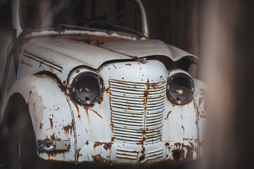a rusty, broken-down white car with no headlights