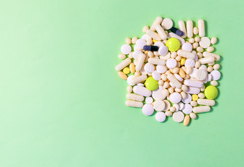 Many colored tablets on a green background. Copyspace for text. Epidemic, pain relievers, health care, medical pills. The concept of drug abuse. Top view