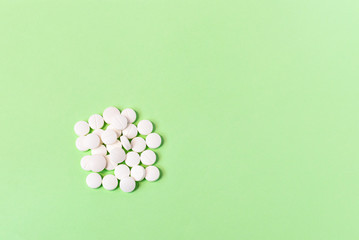 A bunch of white pills on a green background. Health care, epidemic, painkillers, medications and pills. The view from the top. copyspace for text