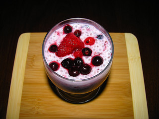Pink milkshake with chia seeds and berries (black and red currant, strawberry) on a wooden board