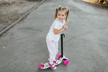 Little girl with pigtails and hairpins on her hair, a child riding a multi-colored scooter, holding the wheel. Photography, concept.