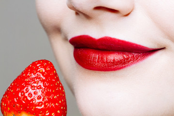 Macro close up of caucasus woman's lips with red lipstick and fresh strawberry.