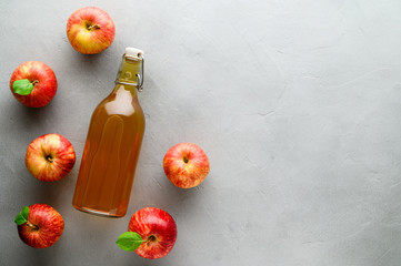 Homemade fermented kombucha or cider in a bottle and red apples on a gray stone background. A healthy probiotic refreshing drink is kombucha. Copy space, top view.