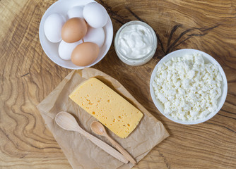 Rustic products on a textured wooden table: cottage cheese, eggs, sour cream and cheese. Healthy food, a source of natural calcium and vitamin D