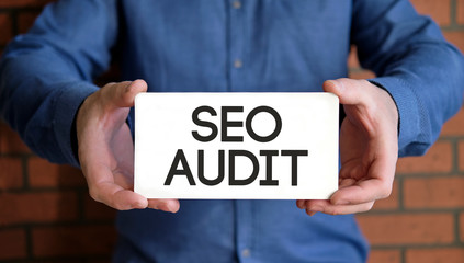 Seo audit text on a white sign in two hands of a man in a blue shirt